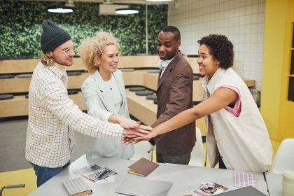 Gemischtes Team aus Männern und Frauen legt im Büro die Hände zusammen als Symbol für Zusammenarbeit.